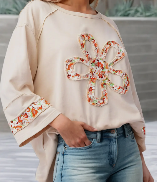 A beige colored loose top with a floral pattern and wide sleeves, worn by a person paired with blue jeans.