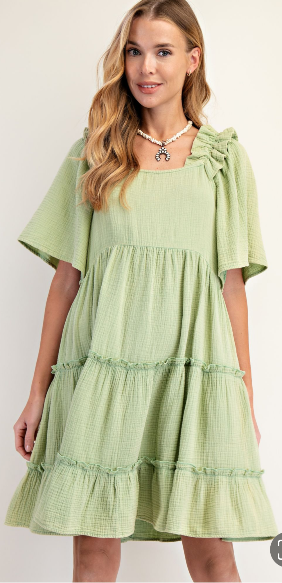 A woman wearing a green short sleeve mini dress with ruffles and a round neckline.