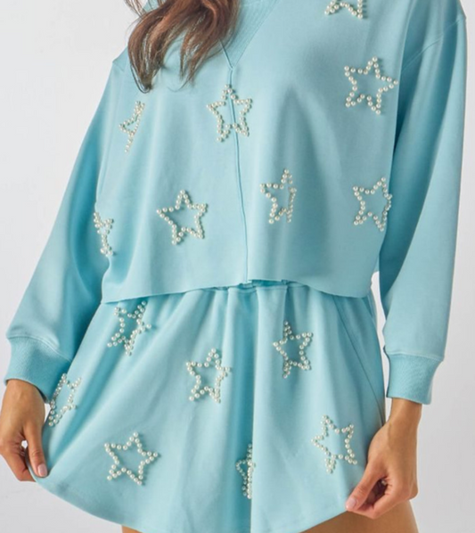 A blue pullover top with faux pearl star outlines on the sleeves, rib neck and cuffs, and a cropped fit.